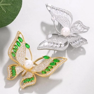 Broche papillon de luxe en or et argent avec pierres vertes et perles sur fond texturé