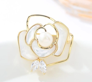 Macro shot of camellia brooch with white petals, gold trim, large pearl and zircon leaves