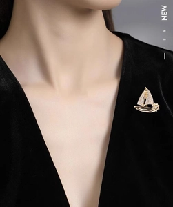 Detail of elegant gold sailboat brooch featuring sparkling crystals on black velvet clothing