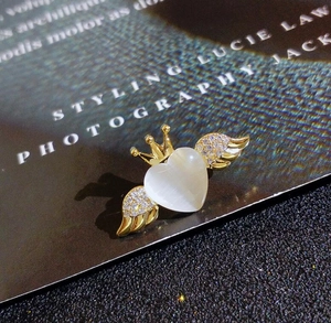 Detail of angel wing brooch featuring opal heart center, gold crown, and crystal accents