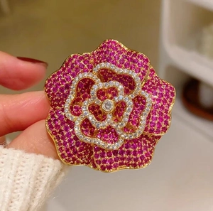 Vue macro montrant les pétales superposés rouge rose et les cristaux de la broche camélia