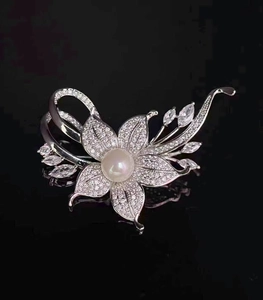 Detail einer silbernen Blumenbrosche mit großer weißer Perle und funkelnden Zirkonias