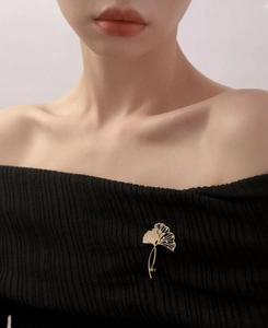 Detailansicht einer goldenen Ginkgoblatt-Brosche mit Glitzersteinen auf schwarzem Pullover