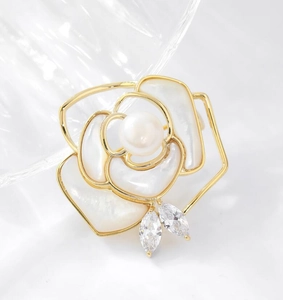 Macro detail of camellia brooch with white shell petals and a pearl center