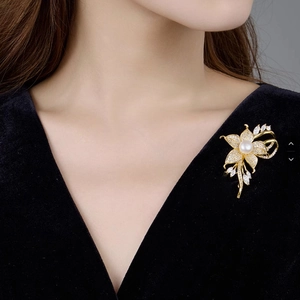 Eleganter goldener Blumenanstecker mit weißer Perle und Kristallen an einem Sakko
