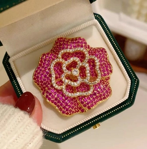 Gros plan d'une élégante broche camélia rouge rose avec strass dans un écrin en velours vert