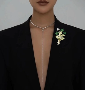 Dettaglio della spilla a bouquet dorata con gemme verdi e perle su un blazer nero elegante
