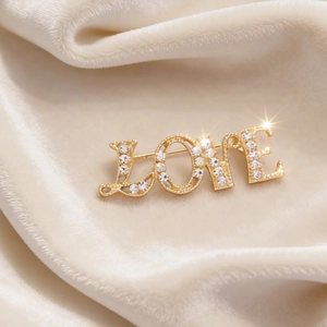 Elegant gold LOVE letter brooch with sparkling pavé crystals on soft beige velvet fabric