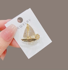 Macro shot of gold sailing boat brooch with crystal zircons and nautical helm detail