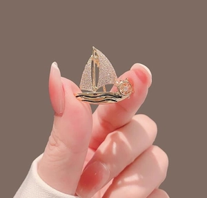 Detailed view of a golden sailboat brooch with sparkling crystals held in hand