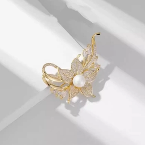 Detail der Blumenbrosche mit großer weißer Perle und funkelnden Kristallen auf Goldmetall