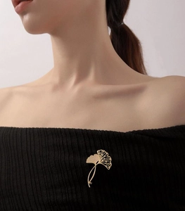 Detail der eleganten goldenen Ginkgoblatt-Brosche mit feiner Textur auf schwarzem Kleid