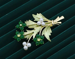 Dettaglio di elegante spilla a bouquet dorata con pietre verdi e grappoli di perle