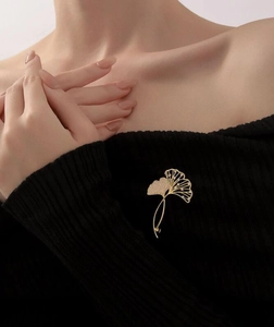 Detail einer luxuriösen goldenen Ginkgo-Brosche mit funkelnden Kristallen auf schwarzem Pulli