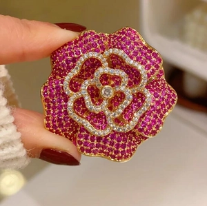 Élégante broche camélia rose rouge avec strass et base dorée en vue macro tenue à la main