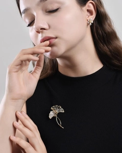 Detail einer luxuriösen goldenen Ginkgo-Brosche und Perlenblumen-Ohrringen an einem Model