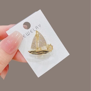 Elegant gold sailboat brooch featuring sparkling white rhinestones and a helm detail