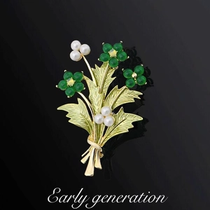 Elegante spilla a bouquet dorata con perle verdi e bianche su sfondo nero sfumato