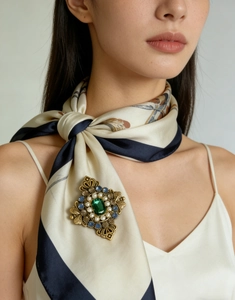 Dettaglio di spilla vintage con smeraldo su sciarpa di seta e abito elegante