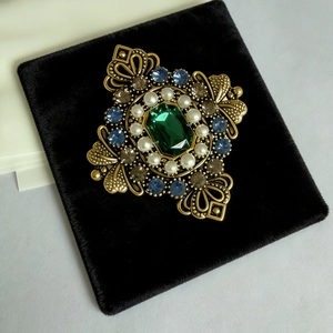 Spilla vintage dorata con gemma smeraldo e perle su velluto nero elegante