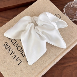 Lustrous white satin bow scrunchie accessory displayed on a vintage linen book cover