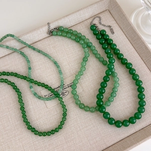 Trois colliers de perles en pierre naturelle verte présentés sur un plateau à bijoux en lin