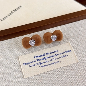 Close-up of brown velvet bow earrings with a heart-shaped rhinestone on linen