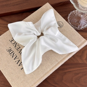 Detail of white satin bow scrunchie with silky texture on a decorative book background
