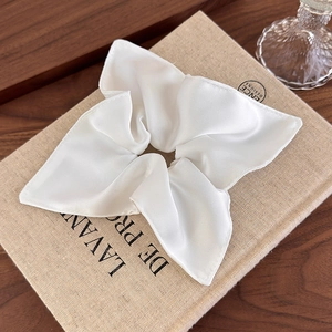 Detail of white satin square scrunchie with silky luster on a vintage book background