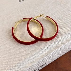 Détail de boucles d'oreilles créoles dorées en velours rouge sur fond de livre ancien