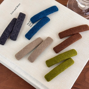 Minimalist plush rectangular hair clips in 5 colors on a cream textured book surface