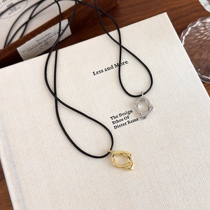 Colliers à pendentifs géométriques or et argent sur cordons noirs posés sur des livres