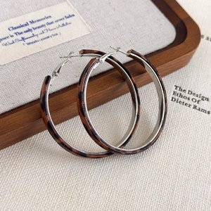 Detail of leopard print hoop earrings with silver finish in a wooden jewelry tray