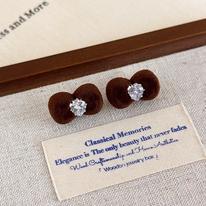 Close-up of brown flocked bow earrings with heart-shaped zircon on aesthetic card