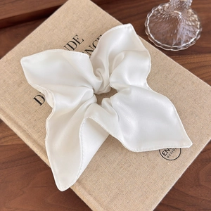 Close-up of pearl white satin oversized scrunchie on a book over wooden surface
