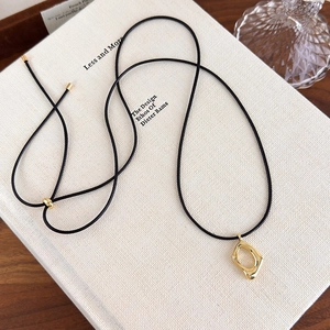Détail d'un pendentif doré minimaliste sur un cordon noir fin posé sur un livre de design
