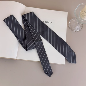 Classic grey striped narrow necktie for women placed on an open book in a minimalist setting