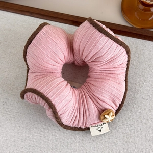 Dettaglio dell'elastico in maglia rosa con bordo marrone, bottone in legno e stella
