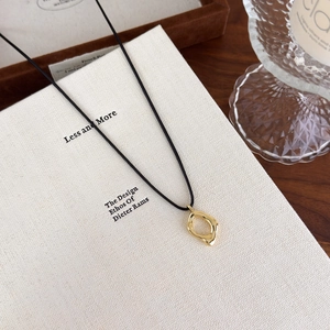 Détail du pendentif géométrique doré creux avec cordon noir sur plateau en bois