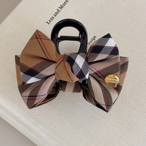 Detail of fabric plaid bow hair claw with engraved gold metal logo plate and pattern