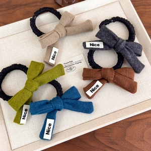 Detail showing five knitted bow scrunchies in various colors with Nice labels