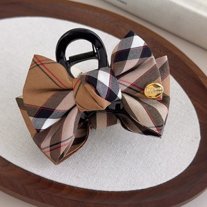 Detail of vintage plaid bow hair claw clip with golden emblem on a wooden tray