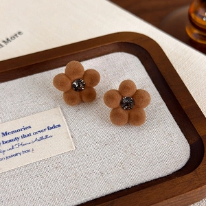 Macro shot of brown flocked floral earrings with sparkling rhinestone center on white tray