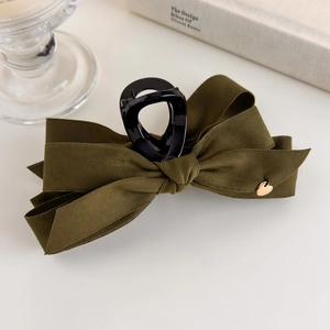 Detail of olive green velvet bow hair claw clip with golden heart accent on white table
