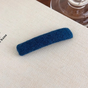 Detail view of a navy blue textured fabric hair clip on a beige book background