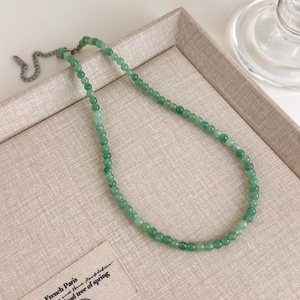 Gros plan du collier en perles de gemme verte avec chaîne réglable en argent sur lin