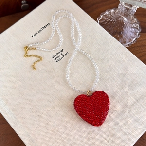 Détail du pendentif cœur en cristal rouge avec chaîne perlée transparente sur un livre