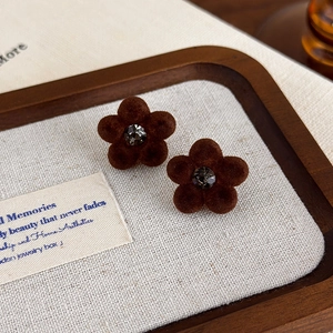 Macro view of brown flocked flower earrings with rhinestone center on linen fabric