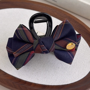 Detail of British style navy blue plaid bow hair claw with gold metal emblem on fabric