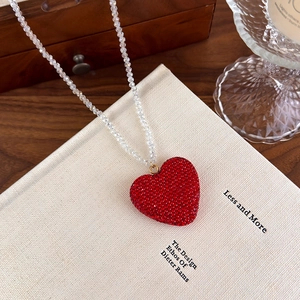 Détail du pendentif cœur en cristal rouge et chaîne en perles irisées sur livre rétro